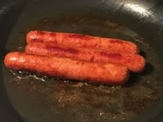 two sausages are cooking in a frying pan