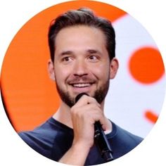 a man with a beard holding a microphone in front of an orange and white background