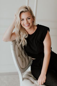 a woman sitting in a chair with her hand on her head and smiling at the camera