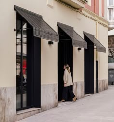 a woman is walking down the sidewalk in front of some storefronts with black awnings