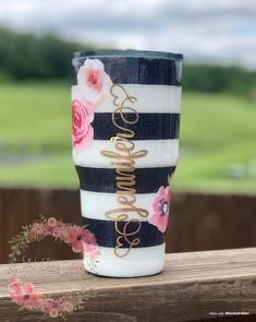 a black and white striped coffee cup with pink flowers on the side sitting on a wooden table