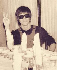 a man wearing sunglasses sitting at a table with candles in front of him and making the peace sign