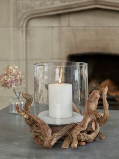 a candle is sitting in a glass vase with driftwood pieces around it on a table