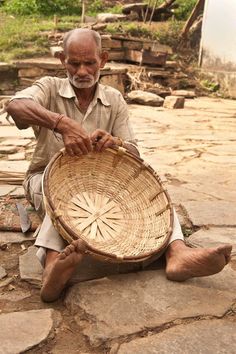 an old man sitting on the ground holding a basket