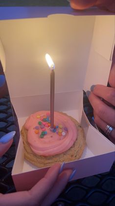 a pink frosted birthday cake in a box with a lit candle sticking out of it