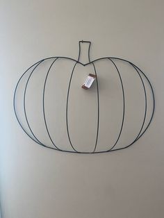 a wire pumpkin hanging on the wall with a tag attached to it's side