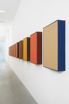 a row of colorful paintings hanging on the side of a wall next to a hallway