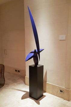 a blue sculpture sitting on top of a black pedestal in a room with white walls