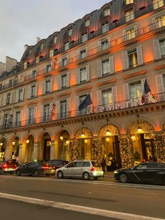 cars are parked in front of a hotel at night with lights on the windows and balconies