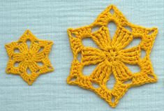 two yellow crocheted squares are on a blue surface, one has an intricate design