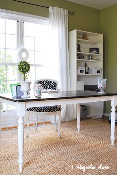 a white table sitting in front of a window next to a chair and bookshelf