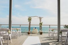 an outdoor wedding setup with white chairs and flowers on the aisle, overlooking the ocean