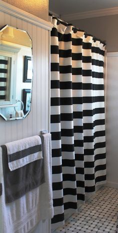 a black and white striped shower curtain in a bathroom next to a sink with a mirror on the wall