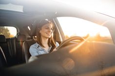 a woman sitting in the driver's seat of a car smiling at the camera