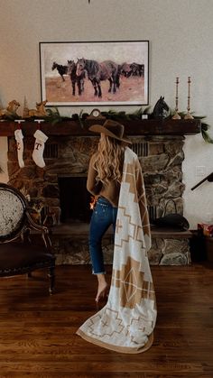 a woman standing in front of a fireplace with a blanket over her head and horses on the mantle