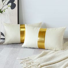 two white and gold pillows sitting on top of a bed next to a vase with flowers