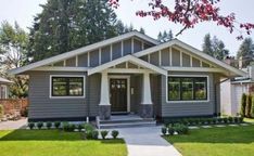 a gray house with white trim on the front and side windows, trees in the background