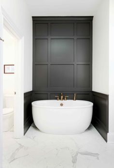 a large white bath tub sitting in a bathroom next to a toilet and wall with black paneling