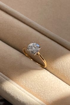 a diamond ring sitting on top of a beige velvet seat in a room with light coming through the window