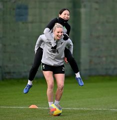 two women are playing soccer on the field with one woman in mid air, while the other holds her