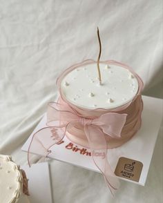 a white cake with pink ribbon and a single twig sticking out of it