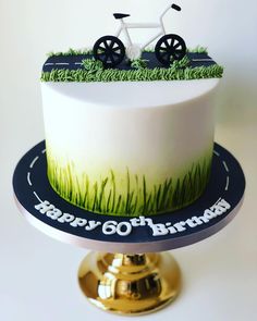 a birthday cake decorated with grass and a bike on it's top tier is sitting on a gold plate