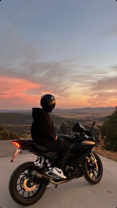 a person sitting on a motorcycle with the sun setting in the back ground behind them