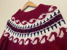 a red sweater with white and blue designs on the front is hanging from a wooden hanger