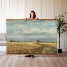 a woman holding up a large painting in front of her face