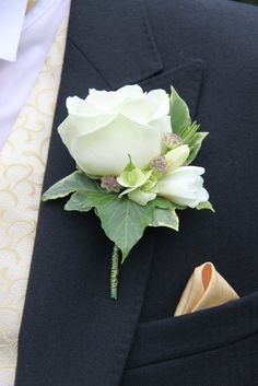 a boutonniere with white roses and greenery is worn on the lapel of a man