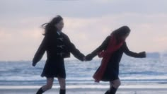 two girls are walking on the beach holding hands