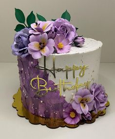 a birthday cake decorated with purple flowers and gold lettering