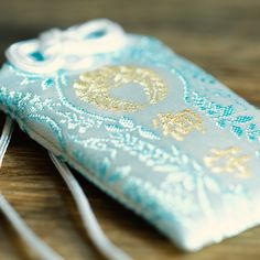 a blue and white bag with gold designs on it sitting on a wooden table next to a cell phone