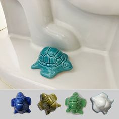 three different colored turtle shaped soaps sitting on top of a white toilet bowl next to each other