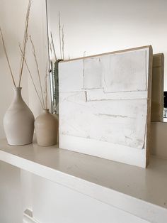 two vases are sitting on a shelf next to a white painted wooden sign and mirror