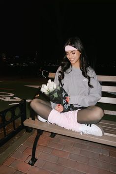 a woman sitting on a bench with flowers in her hand and stockings around her ankles