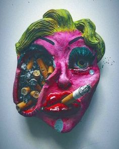 a pink mask with green hair and makeup on it's face is covered in crayons