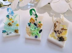 three soap bars with flowers on them sitting next to each other in front of white flowers