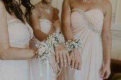 three bridesmaids in pink dresses hold bouquets of flowers and pearls on their hands