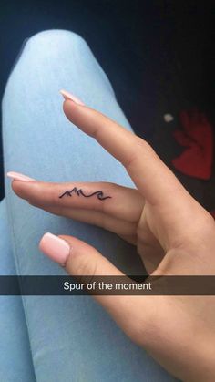 a woman's hand with a small wave tattoo on her left thumb and the words, spur of the moment