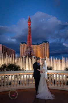 a bride and groom pose in front of the fountains of water at their las vegas wedding