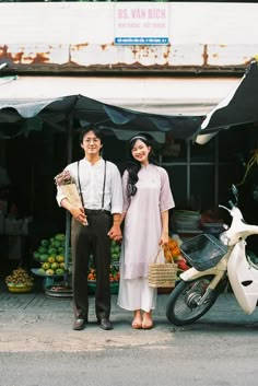 a man and woman standing next to each other in front of a motorcycle with fruit on it