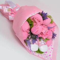 a bouquet of pink flowers and baby shoes is wrapped in paper on a white surface