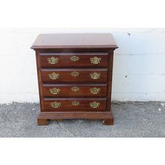 an antique chest of drawers with brass hardware on the top and bottom, against a white brick wall