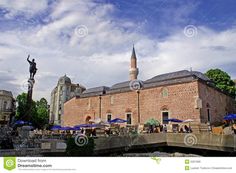 an old brick building with blue umbrellas and people sitting at tables in the foreground