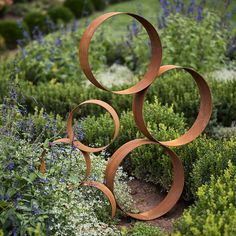 a metal sculpture sitting in the middle of a garden filled with purple and white flowers