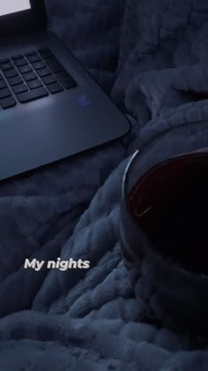 an open laptop computer sitting on top of a bed next to a glass of wine