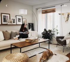 a woman sitting in a living room reading a book with her dog laying on the floor