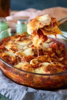 someone is taking a piece of lasagna out of the casserole dish