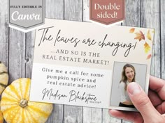 a person holding up a real estate card with pumpkins and squash in the background